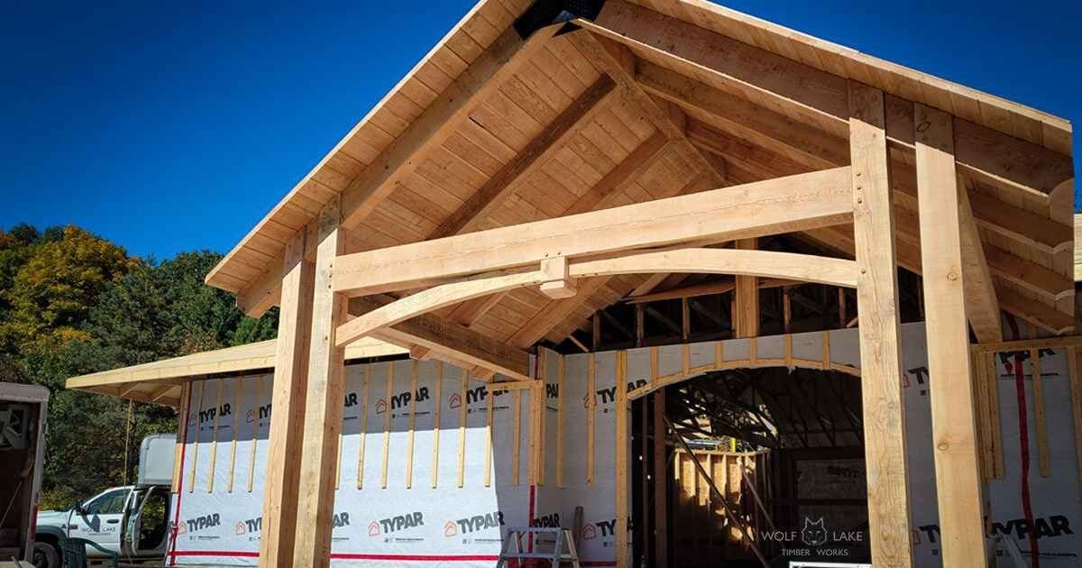 Timber framing under construction with exposed beams against a clear blue sky.